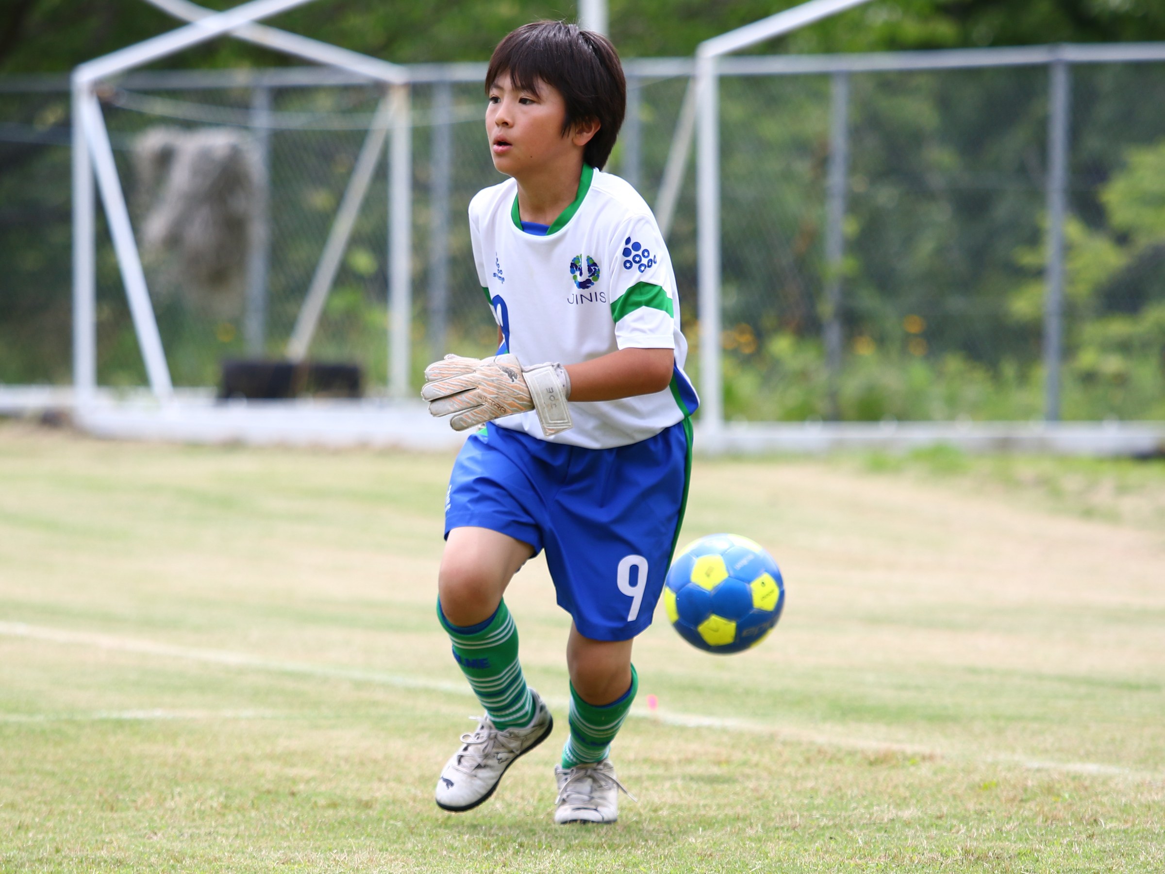 A goalkeeper bringing the ball out on the school pitch
