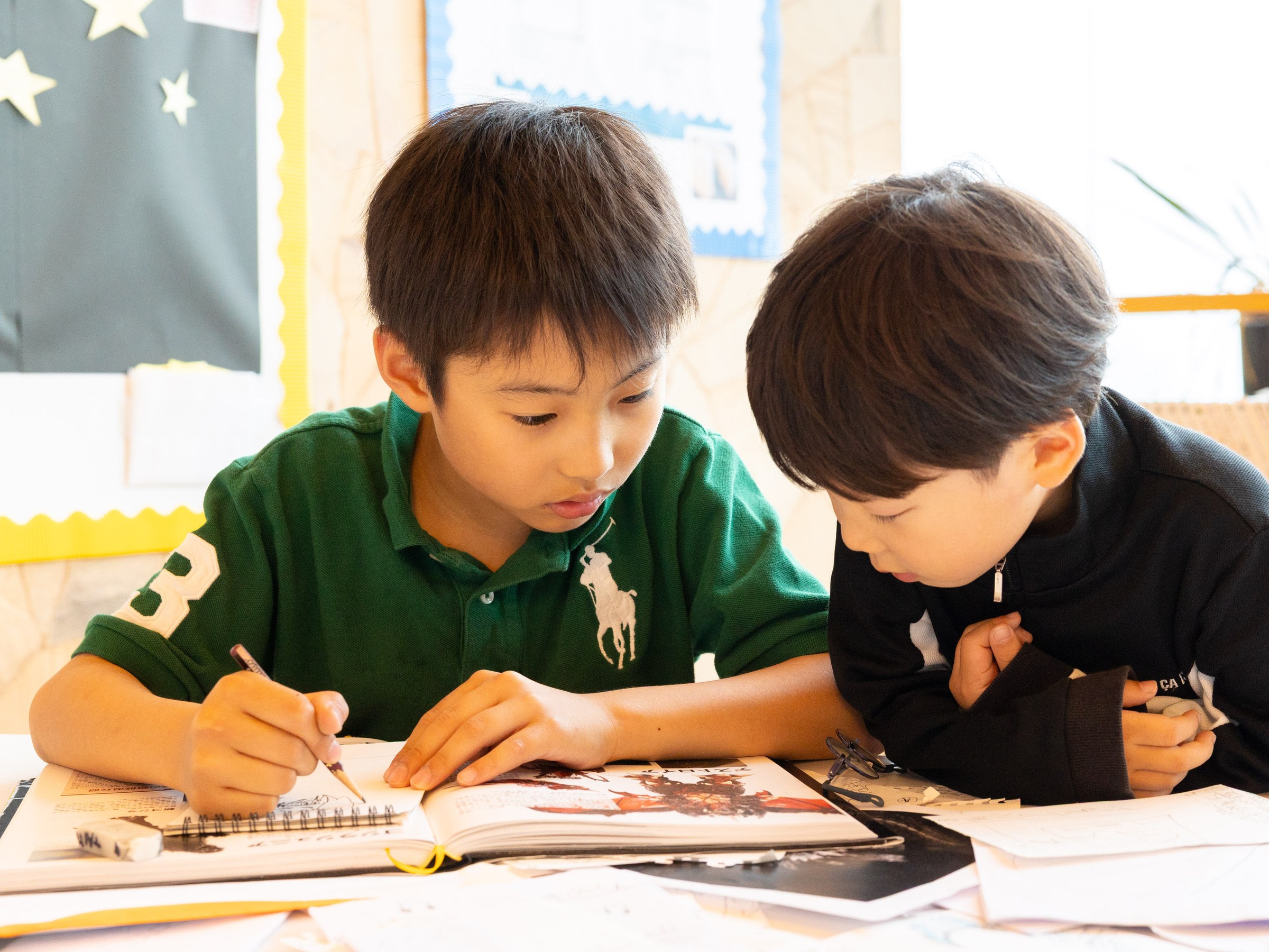 Two pupils working over an open sketchbook in a classroom